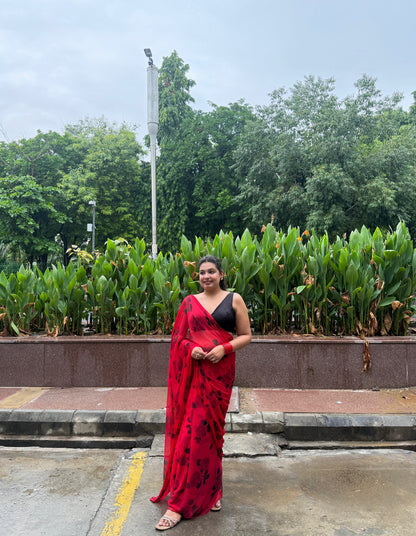 Woman in a red saree standing outdoors with greenery in the background