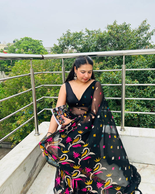 Woman in a black and colorful traditional outfit on a balcony with greenery in the background