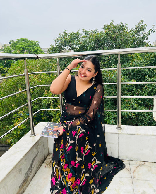 Woman in a black floral saree on a balcony with green trees in the background