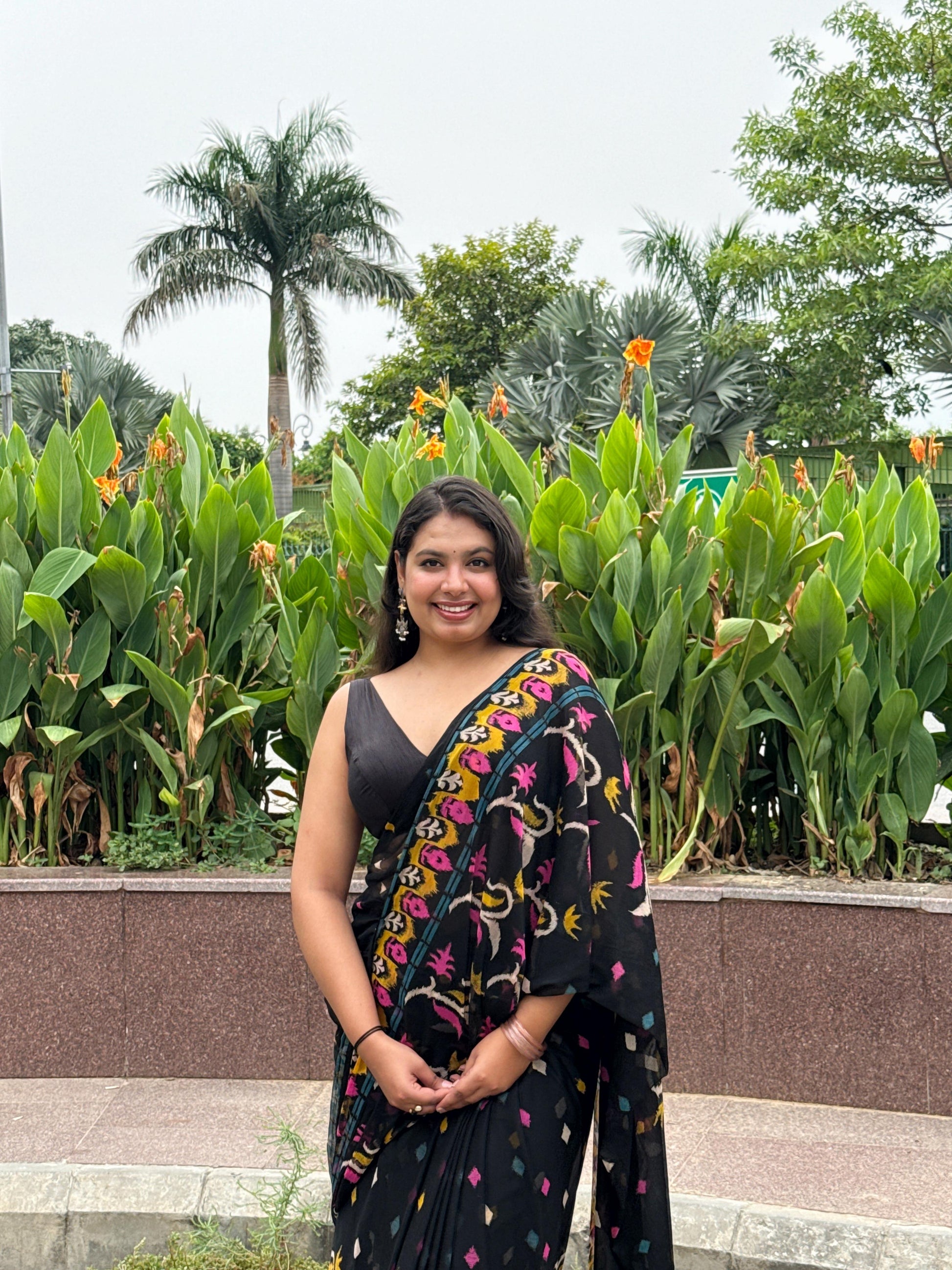 Woman in a colorful saree standing in front of green plants